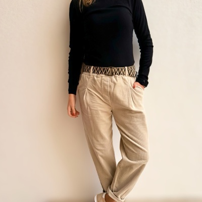 Pessoa vestindo blusa preta, calças bejes de veludo cotelê com cinto estampado e sapatilhas bege com riscas brancas.