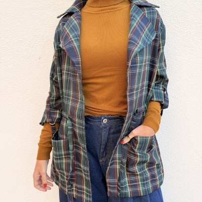 Pessoa a usar camisola castanha, casaco tartan verde e calças de ganga azuis