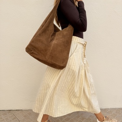 Mulher com saco castanho em tecido camurça, camisola castanha, saia creme às riscas e ténis bege com riscas brancas