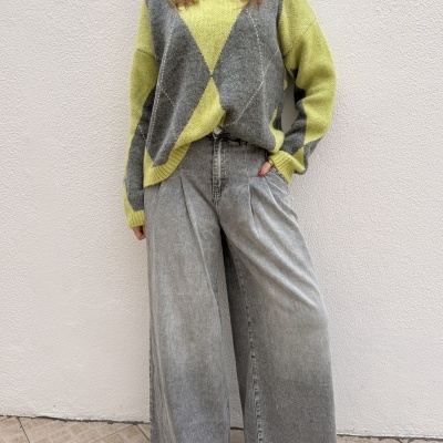 Pessoa com camisola argyle amarela e cinza, calças largas de ganga cinzentas e ténis brancos em fundo branco