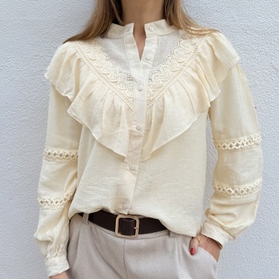 Camisa creme com folhos e rendas, calças bege e cinto castanho com fivela dourada