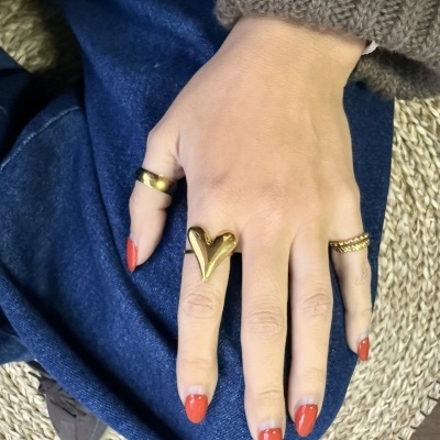 Mão feminina com três anéis dourados e unhas vermelhas sobre tecido azul e ráfia