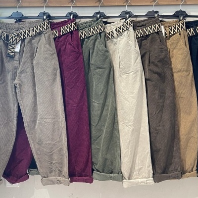 Sete calças de veludo cotelê em várias cores com cintos tecido e padrão geométrico penduradas numa barra de madeira