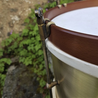 Tambor com aro de madeira, corpo metálico dourado e pele branca ao ar livre