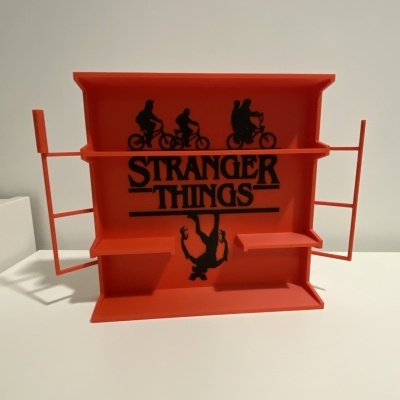 Organizador plástico laranja com texto STRANGER THINGS e silhuetas pretas de bicicletas e figura pendurada.