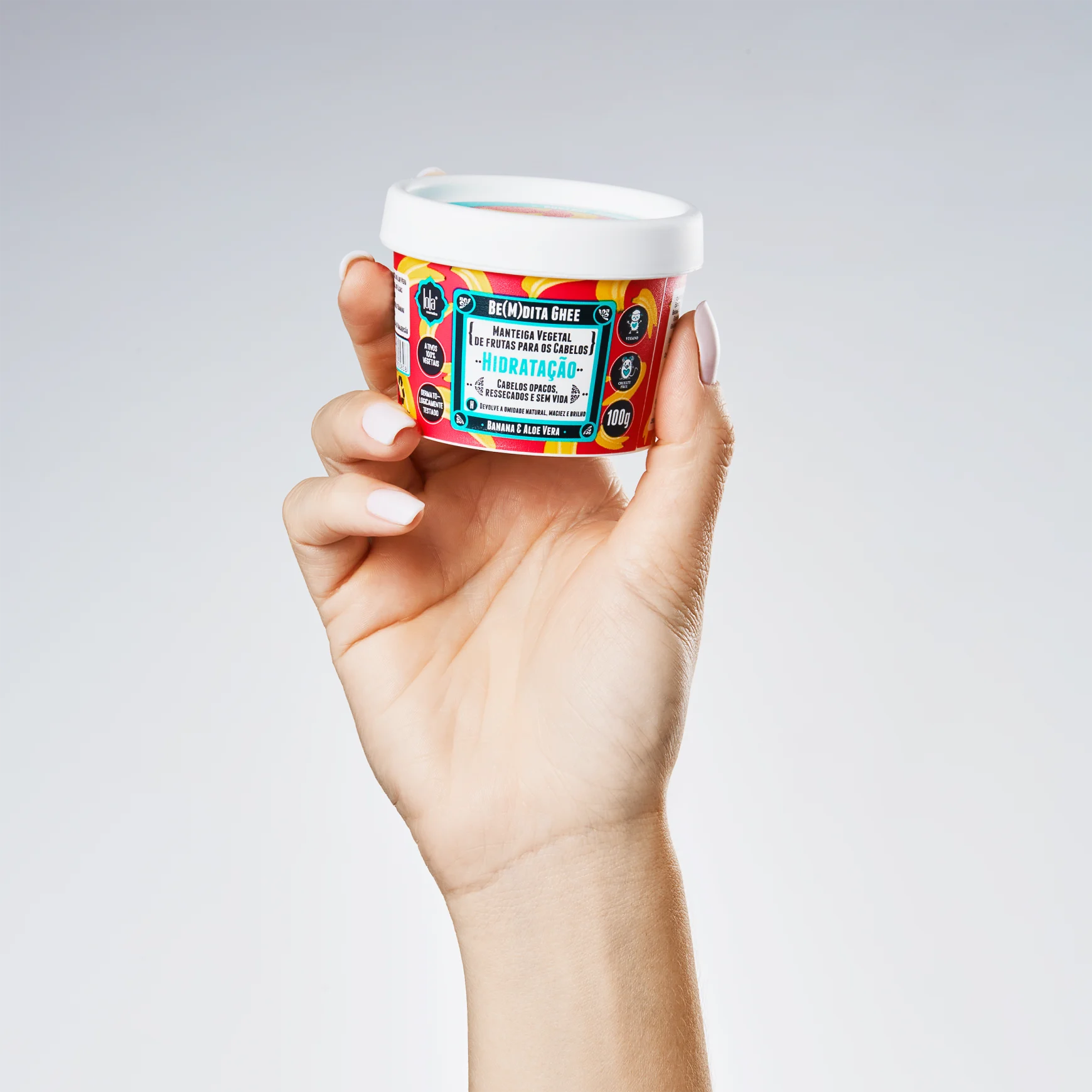 Mão segurando creme hidratante facial em frasco branco com rótulo colorido