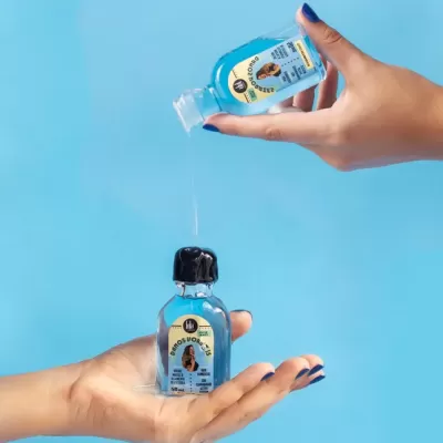 Frascos de álcool gel com rótulos azuis em mãos sobre fundo azul.