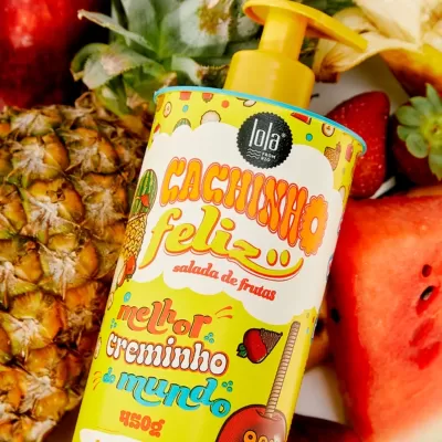 Frasco amarelo de produto 'Cachinho feliz salada de frutas' com tampa de bomba sobre frutas naturais