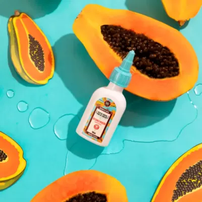 Garrafa branca com tampa azul entre metades de papaia com sementes pretas em fundo azul