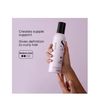 Frasco branco com tampa preta de produto para cabelo segurado por mão em fundo lilás