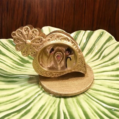 Anel dourado decorativo com padrão floral sobre prato verde em relevo