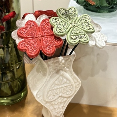 Flores decorativas em cerâmica com texto 'AMOR' num vaso branco com textura