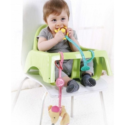 Bebé sentado em cadeira com assento plástico verde e brinquedos coloridos presos com fitas e clips