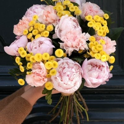 Ramo de flores cor-de-rosa e amarelas segurado por mão diante de fundo preto