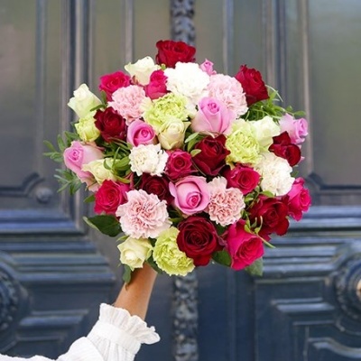 Buquê colorido de rosas e cravos segurado à frente de porta azul decorativa