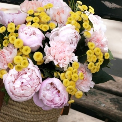 Arranjo de flores com peónias rosa e flores amarelas numa cesta de palha sobre banco de madeira