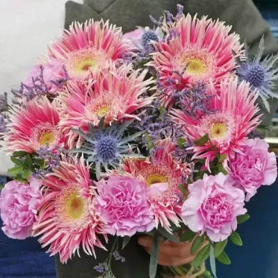 Bouquet de flores rosas com folhas verdes segurado por uma pessoa.