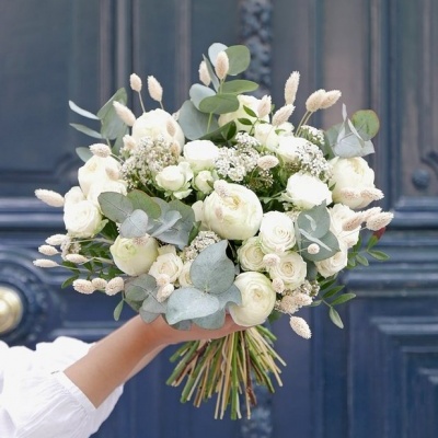 Ramo de flores brancas e verdes segurado em frente a uma porta azul escura