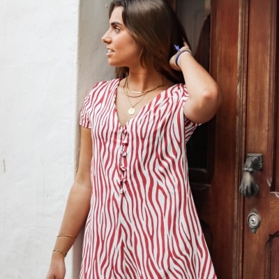 Macaquinho feminino vermelho e branco com padrão de riscas, botões frontais, em ambiente exterior junto a porta de madeira.