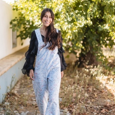 Mulher a usar macacão azul claro floral e blusa preta de folhos a caminhar num caminho de pedras ao ar livre