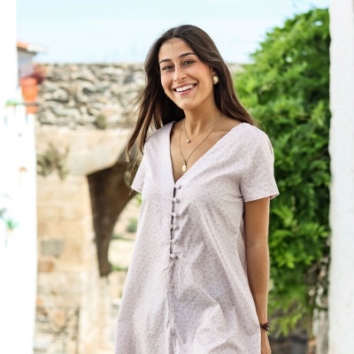 Vestido creme com padrão de flores pequenas e botões na frente, usado por mulher feliz num ambiente exterior rústico.