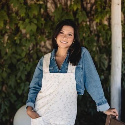 Mulher com macacão branco estampado e camisa jeans azul num ambiente exterior com vegetação