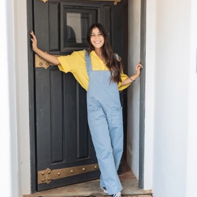 Mulher com jardineira azul e tshirt amarela em porta preta com ferragens douradas