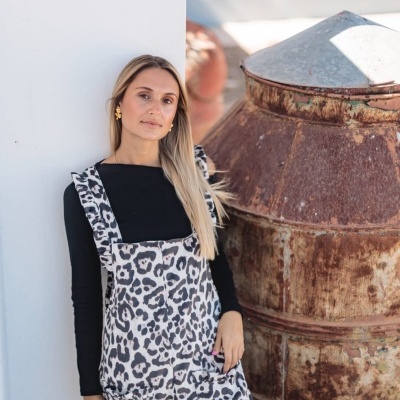 Mulher com macacão animal print preto, branco e cinza ao lado de objeto metálico oxidado