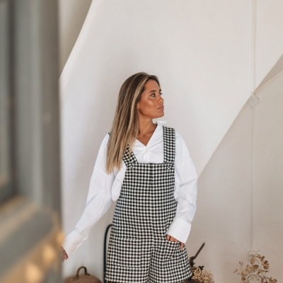 Mulher com macacão xadrez preto e branco e camisa branca em ambiente interior rústico