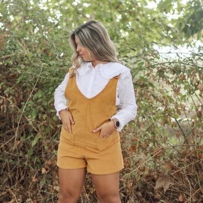 Mulher com macacão amarelo mostarda e camisa branca em ambiente natural
