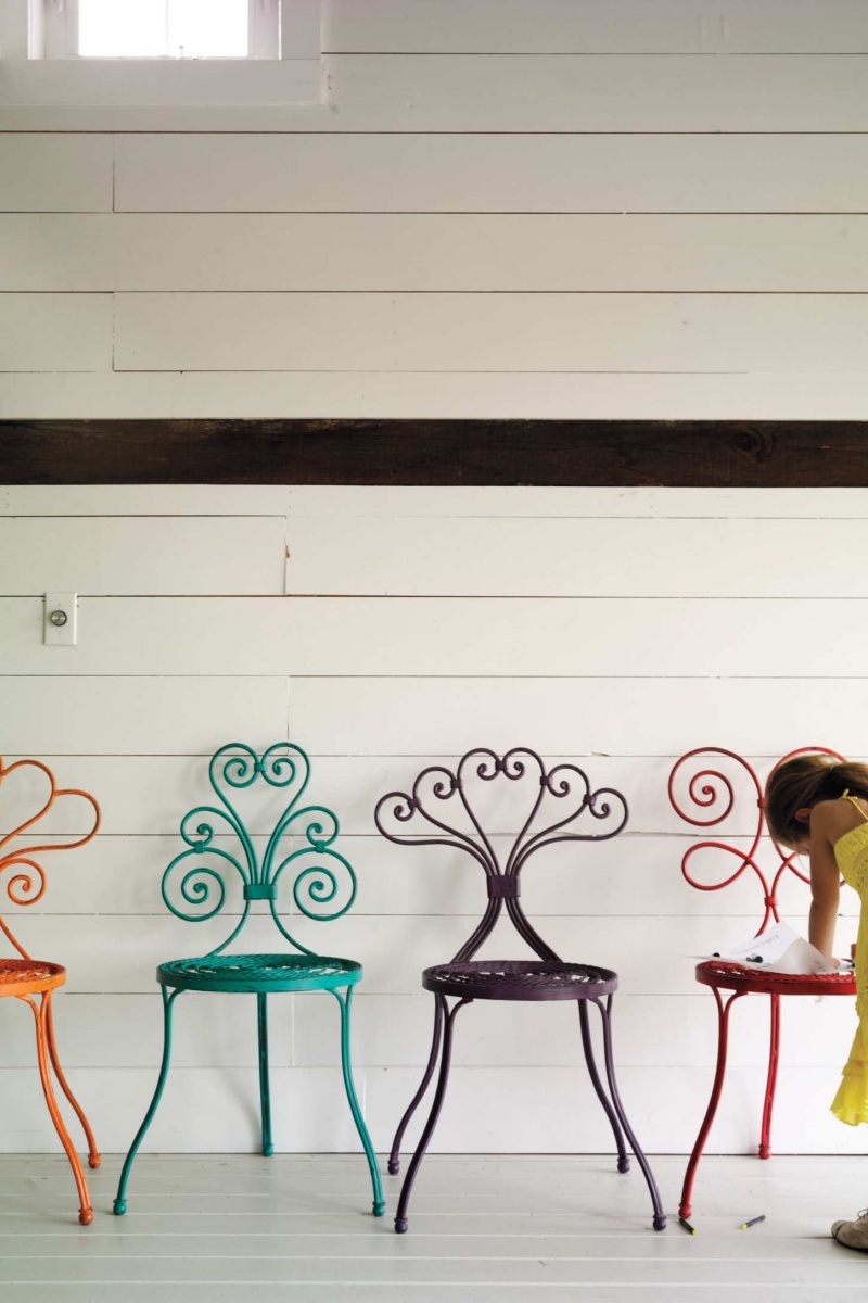 Cadeiras coloridas de ferro com design em espiral contra parede branca e criança interagindo