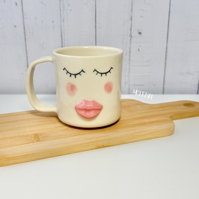 Caneca creme com rosto feminino em relevo e tábua de madeira clara
