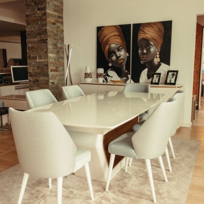 Mesa de jantar branca com oito cadeiras cinzentas em sala decorada com pinturas e paredes brancas