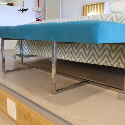 Banco azul turquesa com estrutura metálica prateada em sala com cama padronizada ao fundo