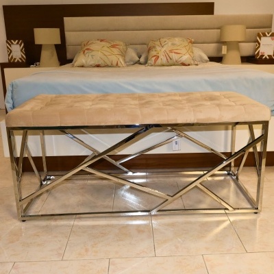 Banco estofado bege com estrutura metálica cromada em quarto com cama de casal