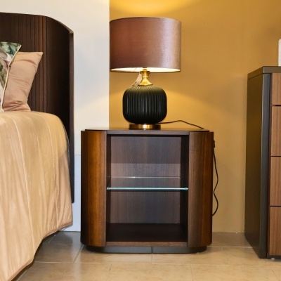 Mesa de cabeceira em madeira com candeeiro ao lado de cama com almofadas