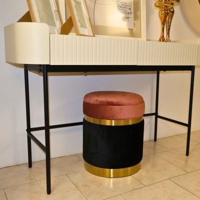 Móvel branco com pés pretos e puff redondo rosa e preto com detalhes dourados num chão de azulejos claros