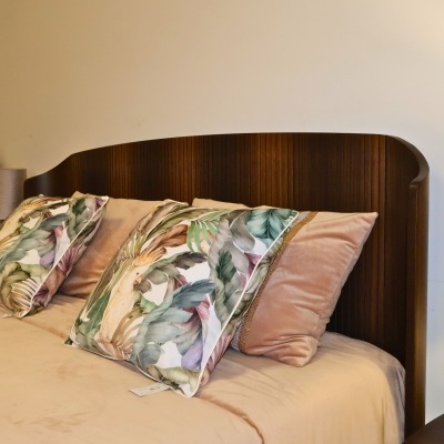 Cama com cabeceira em madeira escura e almofadas com padrão de folhas