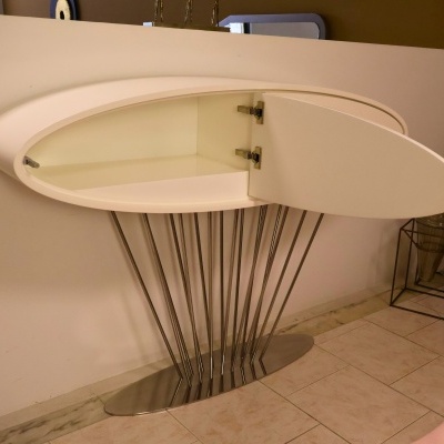 Móvel branco de parede com porta oval aberta e suportes metálicos finos em piso de azulejos.