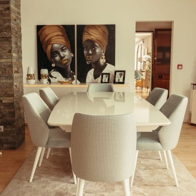 Mesa de refeições branca com seis cadeiras estofadas cinza claro numa sala com arte na parede