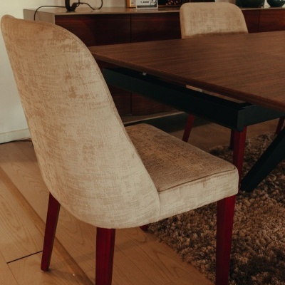 Cadeira estofada bege com pernas em madeira e mesa de madeira escura com tapete castanho.