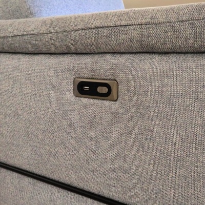Detalhe de sofá cinza claro em tecido com botão de controlo embutido.