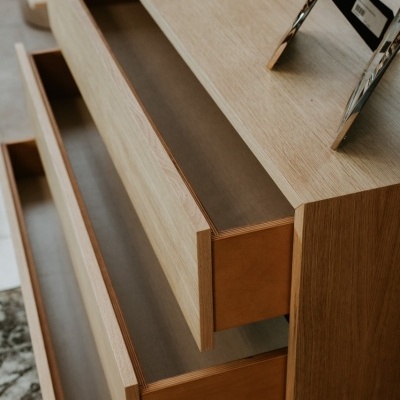 Cômoda de madeira clara com gavetas abertas e decoração no topo