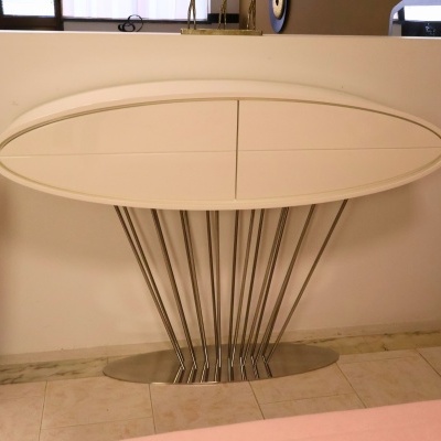 Aparador oval branco com base metálica contra parede branca e chão em mármore