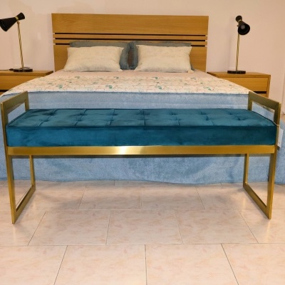 Banco azul de veludo com estrutura dourada em quarto com cama de casal e mesas de cabeceira