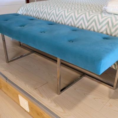 Banco estofado azul com estrutura metálica junto a cama com colcha padrão zig-zag