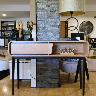 Secretária em madeira clara com pernas pretas e parede de pedra cinzenta ao fundo
