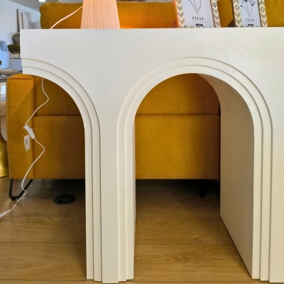 Mesa branca com arcos decorativos e textura áspera junto a sofá amarelo