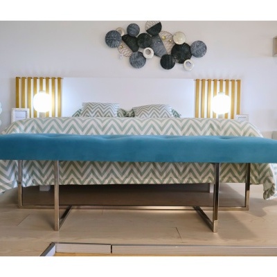 Banco azul com pernas metálicas em quarto com cama branca e decoração na parede