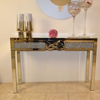 Aparador espelhado dourado com decoração na superfície e em torno, objetos decorativos no topo.